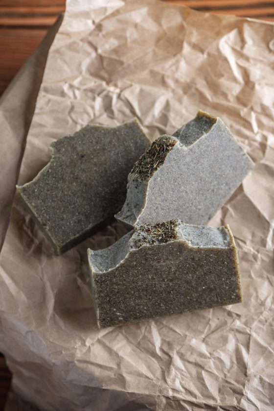 Two bars of handmade cold process soap on kraft paper, cut to show a herb layer through the middle.